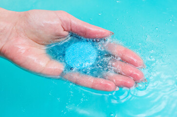 Fototapeta na wymiar Hand of woman, having pampering bath, holding blue fizzing bath bomb.