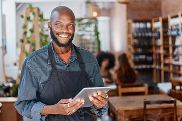 Young african american businessman working in a retail store using a digital tablet device. Portrait of a smiling small business owner, entrepreneur buying stock online using wireless technology