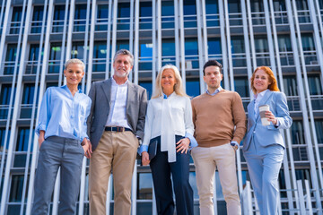 Obraz premium Portrait of cheerful group of coworkers walking outdoors in a corporate office area, with an office building in the background