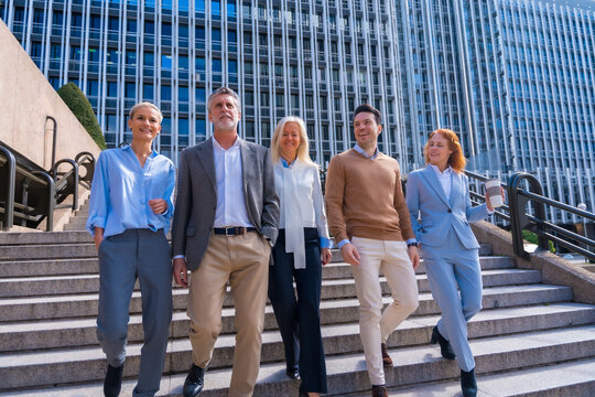 Cheerful group of coworkers outdoors in a corporate office area going down some stairs going to work, businesswoman and businessman