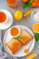 Toasts with orange marmalade or orange jam with cup of tea on a gray background. Delicious breakfast. Copy space.