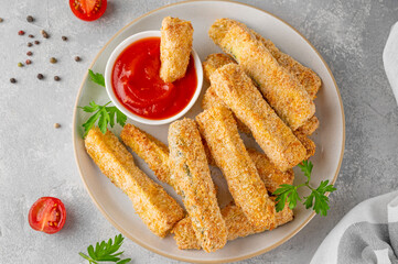 Baked crispy garlic parmesan zucchini sticks served with tomatoes sauce on a gray concrete background. Vegetarian healthy dish. Selective focus.