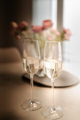 Two glasses of champagne with defocused flowers in the background and softly illuminated windows