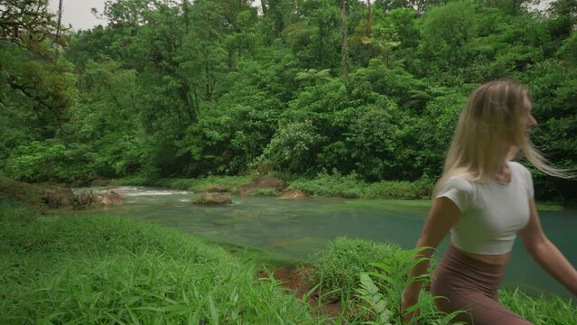 Fit blond woman walking along river bank of serene Rio Celeste in Costa Rica