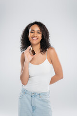 cheerful african american woman holding cosmetic serum and smiling at camera isolated on grey.