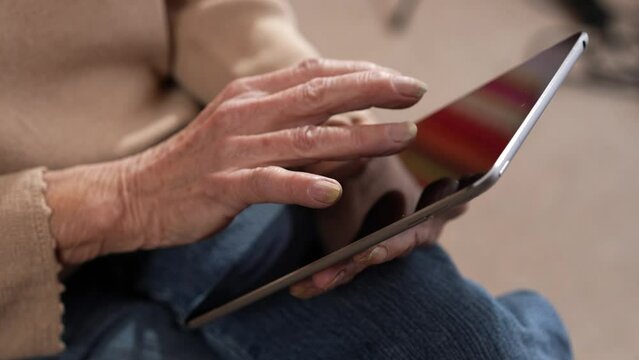 Closeup of senior old elderly womans hands while using touchpad tablet computer with finger to scroll.