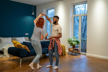 Romantic interracial young family couple wife and husband dancing to music together, smiling and having fun together, spending free time with partner on weekend at home. Happy relationships