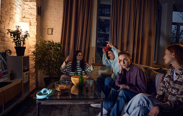 Winners. Young friends, boys and girls sitting on sofa, playing console at home in the evening, online sport, box games. Weekends. Concept of friendship, leisure activity, hobby, fun © master1305