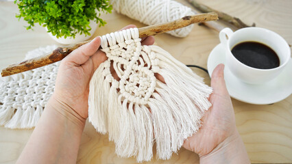 close-up of female hands holding diy macrame an amulet made of white cotton threads on a driftwood...