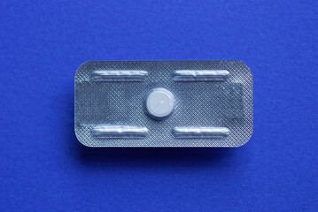 a gray plastic medical blister with one white pill lies on a blue table