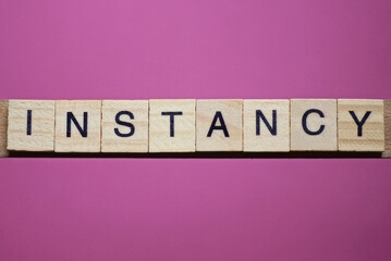 word instancy from small gray wooden letters lies on a purple background
