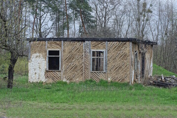 ruins of an old gray brown abandoned house with empty windows in green grass on the street