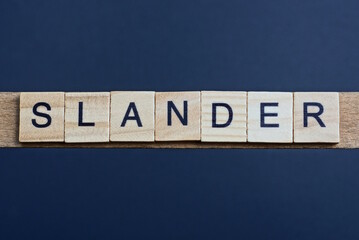 text the word slander from brown wooden small letters on a black table