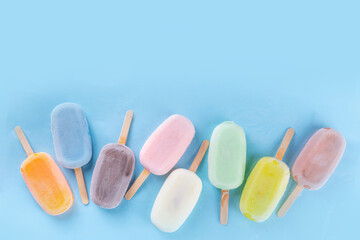 Selection of multicolored ice cream popsicles. Various flavor gelato, frozen lollypops - chocolate vanilla blueberry strawberry pistachio orange, on light blue background
