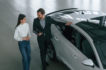 Top view. Man is showing the new automobile to the woman customer in the car dealership