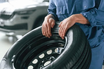 Fototapeta premium Tire replacement concept. Man in blue uniform is working in the car service
