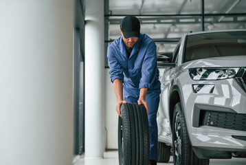 Front view, moving the tire. Man in blue uniform is working in the car service