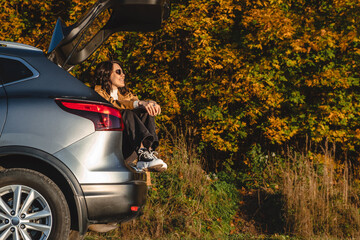 a dreamy woman sits in the trunk of her car and rests from a long journey