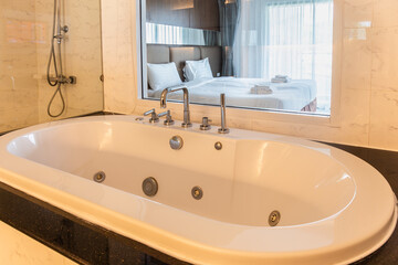 white bathtub with warm lighting against a mirrored backdrop with a bed in the bedroom.