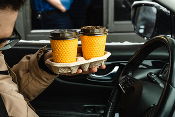 a man in a car holds cups of coffee that he ordered while driving or passing by.