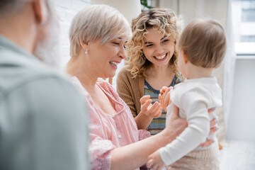 Obraz premium joyful women playing with toddler child at home in living room.