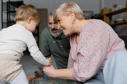 cheerful woman and bearded man playing with little granddaughter at home.