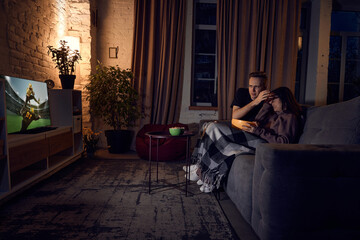 Fototapeta na wymiar Young couple, man and woman spending time together at home in evening, sitting on couch and watching online football match. Loosing game. Concept of friendship, leisure activity, weekends, emotions
