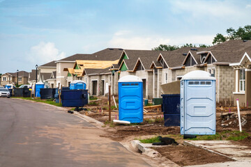 Street view of single-family houses under construction, with dumpsters and portable sanitation...