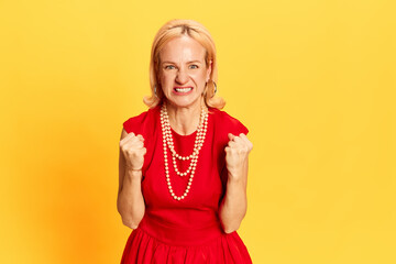 Portrait of pretty woman in red dress rejoices and looking at camera with emotional face on yellow...