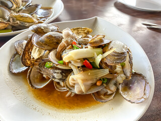 Stir Fried clamps in a white plate bowl on a wooden table. Delicious traditional cooked prawns. Close-up top view high angle.