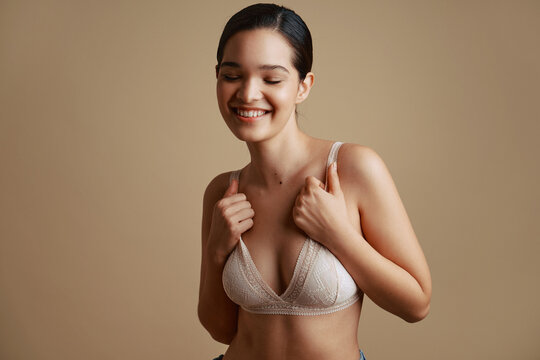 Smiling woman touching bra with closed eyes in studio