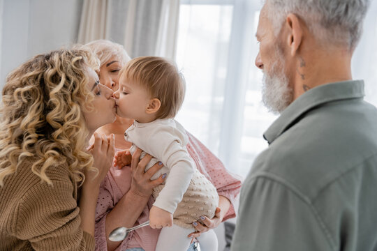 blonde woman kissing beloved daughter near mature parents at home.