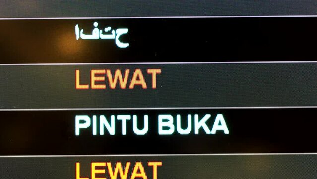 Close-up on airport flight information digital board with focus on word Delayed and Gate Open in English and Malay language