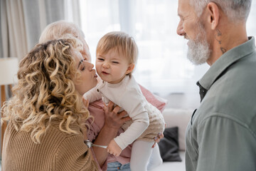 blonde curly woman kissing daughter during visit to mature parents.