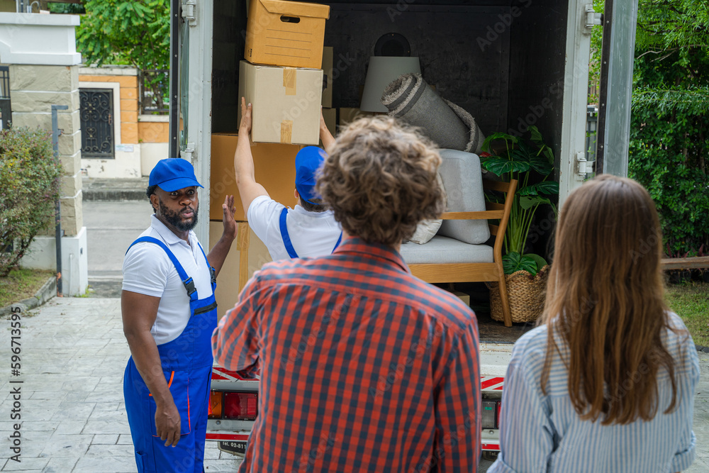 Poster happy couple with moving boxes at new house,moving company employee checks boxes in a truck before s