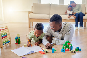 Young happy african american father helping his son with homework while sitting on the floor at home. Little boy focused on learning and doing a task. Small boy drawing in a book