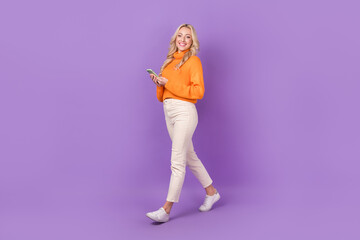 Fototapeta na wymiar Full length profile photo of lovely positive person hold smart phone walking isolated on violet color background