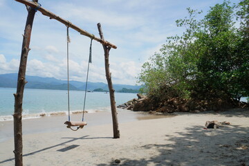 swing at the sandy beach with ocean and mountain landscape as a background