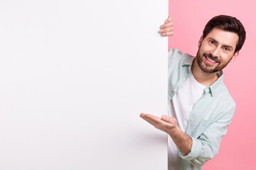 Photo of young funny businessman hiding behind huge placard board demonstrate hand new product name...