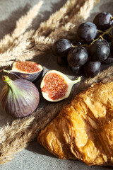 Autumn attributes. Croissant, dark grapes, book and figs on the grey table. Gold October