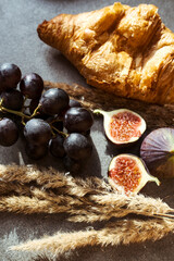 Autumn attributes. Croissant, dark grapes, book and figs on the grey table. Gold October