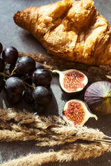 Autumn attributes. Croissant, dark grapes, book and figs on the grey table. Gold October