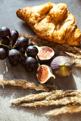 Autumn attributes. Croissant, dark grapes, book and figs on the grey table. Gold October