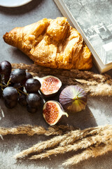 Autumn attributes. Croissant, dark grapes, book and figs on the grey table. Gold October
