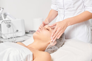 Beautician rubbing moisturizing cream mask into woman face skin for rejuvenation, anti aging...