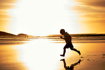 The pilot of a shooting star. Shot of an unrecognizable little boy running along the beach at sunset.