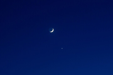 Dark blue clear night sky with the moon and Venus. New growing moon.