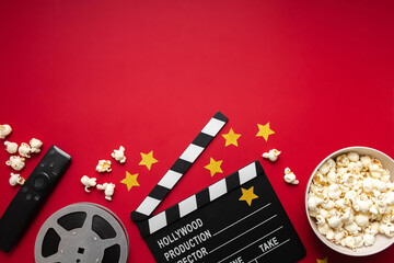 flat lay composition with popcorn, movie clapperboard, film reel and tv remote control on red...
