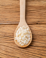 Dried canjica, hominy or white corn in a spoon over wooden table