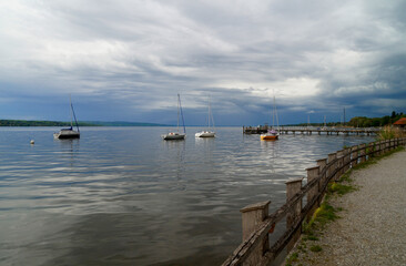 a long wooden pier and sailing boats resting on calm lake Ammersee in Schondorf on an overcast serene evening in spring (Schondorf, Bavaria, Germany)	